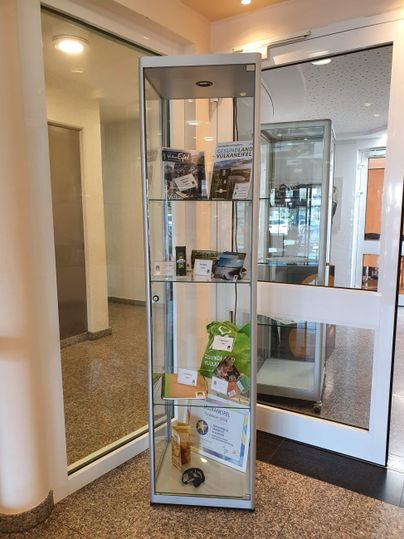 Ein moderner Glasvitrine mit verschiedenen Ausstellungsstücken. Darin befinden sich Broschüren, Produkte und Auszeichnungen.