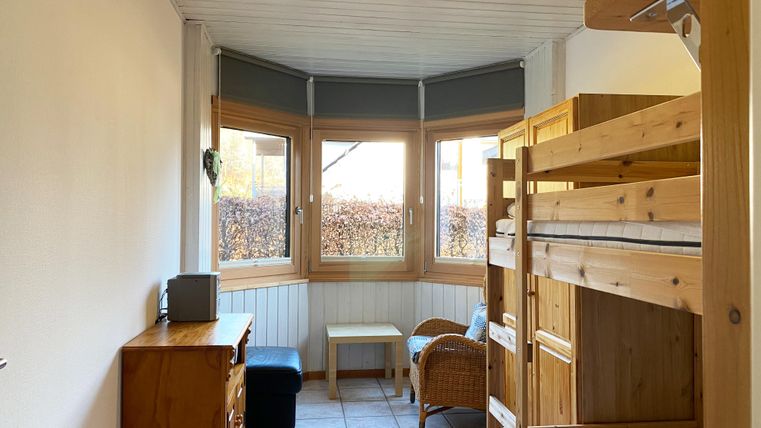 Ein einfaches Zimmer mit einem Etagenbett und einem gemütlichen Sessel. Große Fenster sorgen für viel Licht und Ausblick auf die Außenlandschaft.