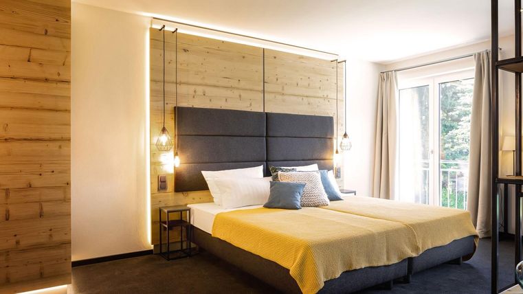 Een moderne slaapkamer met een groot bed en een lichte, minimalistische inrichting. Grote vensters bieden daglicht en uitzicht op buiten.