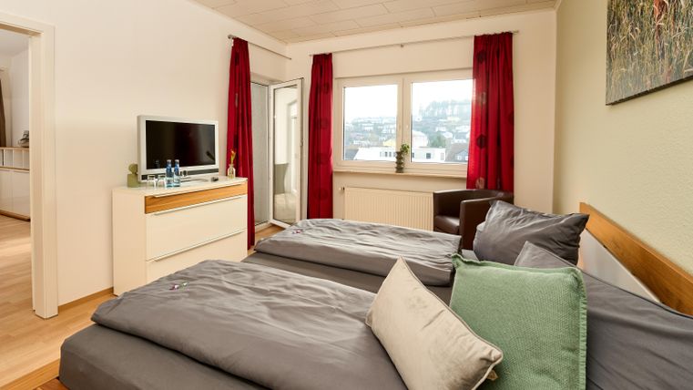 Ein gemütliches Schlafzimmer mit zwei Betten und modernen Möbeln. Große Fenster lassen viel Tageslicht herein und bieten einen Blick nach draußen.