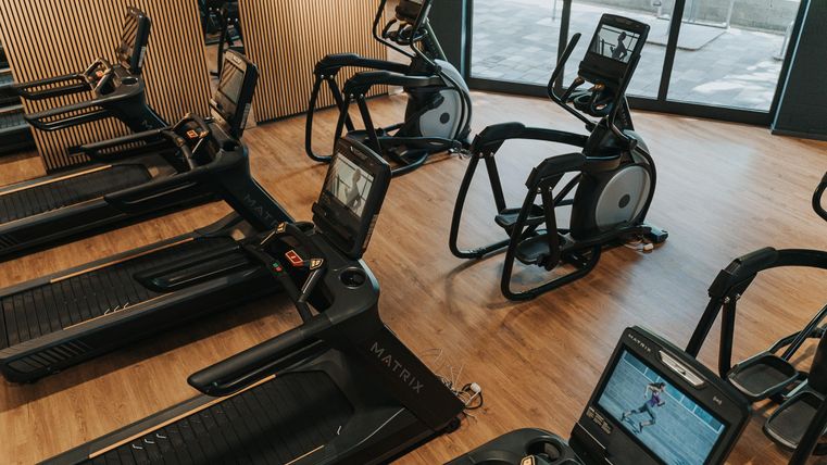Een moderne fitnessruimte met meerdere loopbanden en crosstrainers. De apparaten zijn goed gerangschikt en bieden uitzicht op daglicht.
