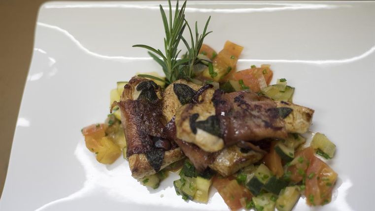 Een gebraden gerecht met kruiden op een bed van verse groenten. Het gerecht is mooi gepresenteerd en ziet er smakelijk uit.