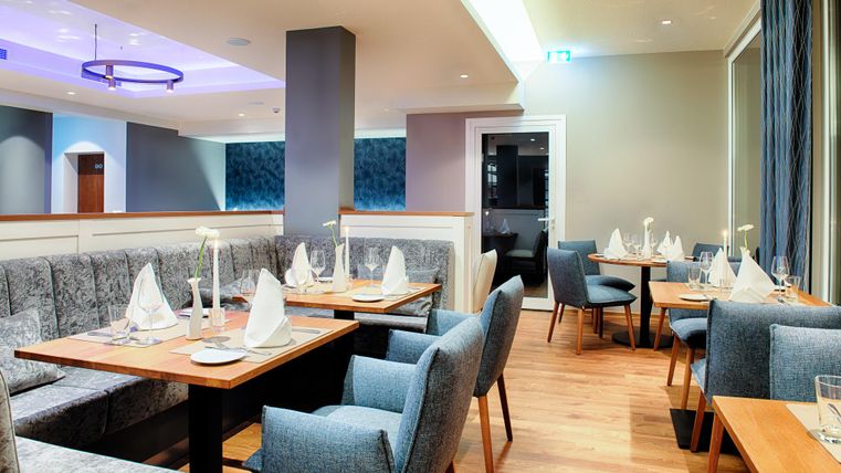 Elegant restaurant met blauwe gestoffeerde meubels, houten tafels en gedekte plaatsen. Moderne verlichting en stijlvolle decoratie.