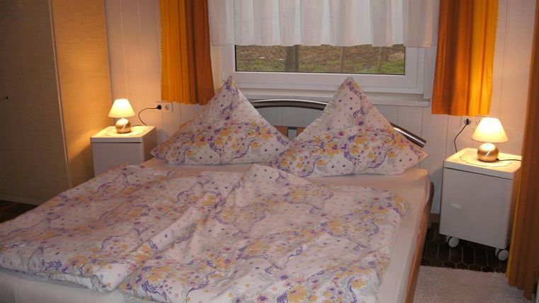 Ein gemütliches Schlafzimmer mit einem großen Doppelbett und bunten Kissen. Die warmen Farben der Vorhänge und Nachttischlampen schaffen eine entspannte Atmosphäre.