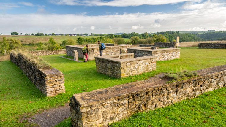 Ruins of an old facility on a green meadow with a view of the surroundings. Two people are exploring the historical stones.