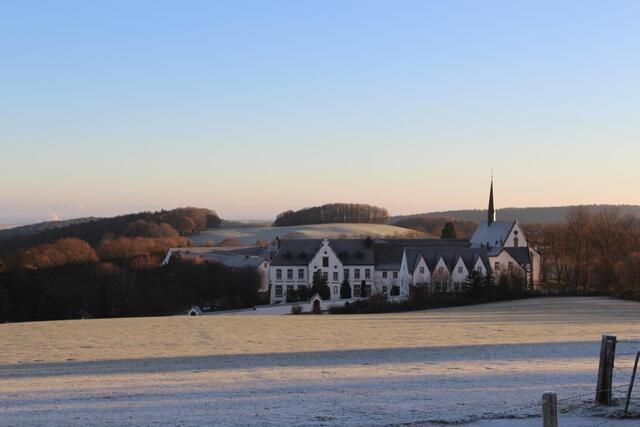 A beautiful landscape with a historic building in the foreground. The meadows are covered with frost and the sky is clear and blue.