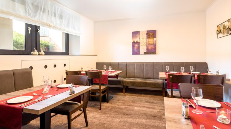 An elegant restaurant with wooden tables and red tablecloths. The walls are decorated, and the lighting creates a pleasant atmosphere.