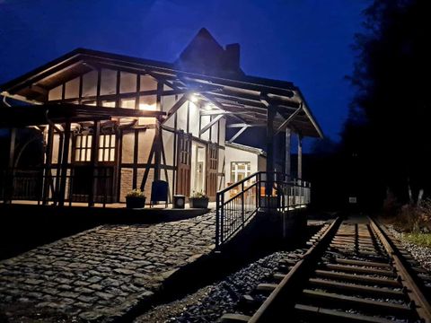 A historic train station park at night, illuminated by warm light. The tracks lead into the darkness, and the building has charming, rustic architecture.