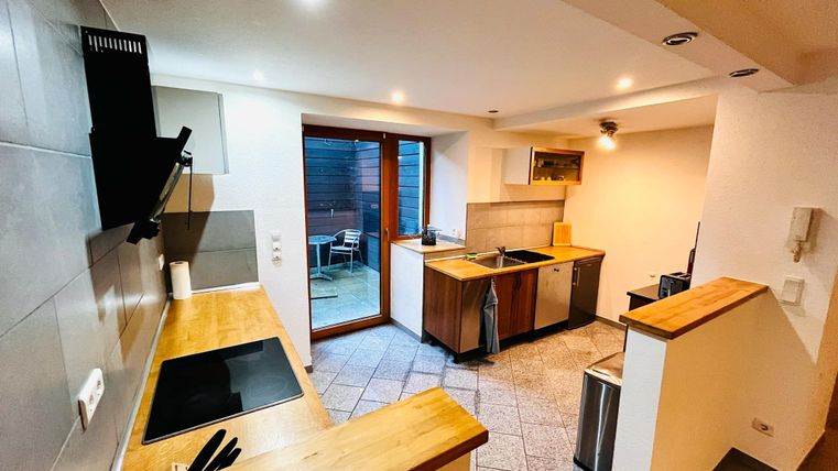 A modern kitchen with wooden surfaces and bright tiles. Large windows provide plenty of light and access to an outdoor area.