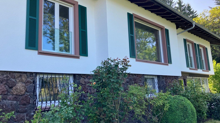 Ein schönes Haus mit weißen Wänden und grünen Fensterläden. Der Garten ist gepflegt und hat viele Pflanzen.