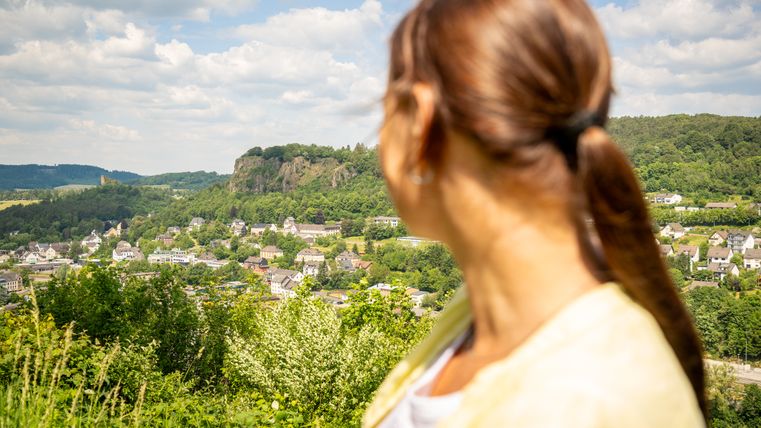 Eine Frau blickt auf eine grüne Landschaft mit einer Stadt im Hintergrund.