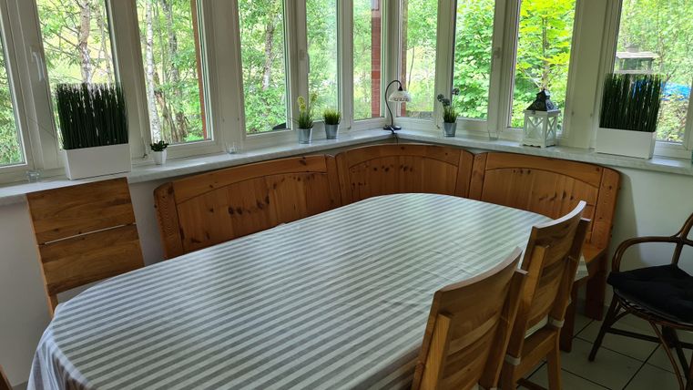 Ein gemütlicher Essbereich mit einem großen Tisch und Stühlen. Die Fenster bieten einen schönen Blick auf die grüne Umgebung.