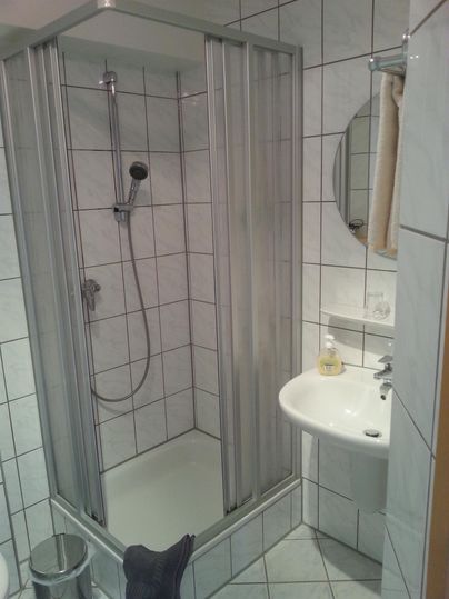 A modern bathroom with a shower and a sink. The walls are tiled and there is a small wall mirror.
