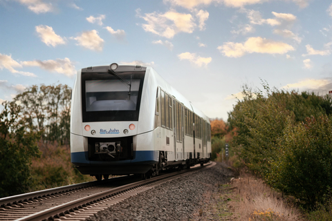 Een trein rijdt over een spoorlijn langs bomen. De lucht is helder met enkele wolken.