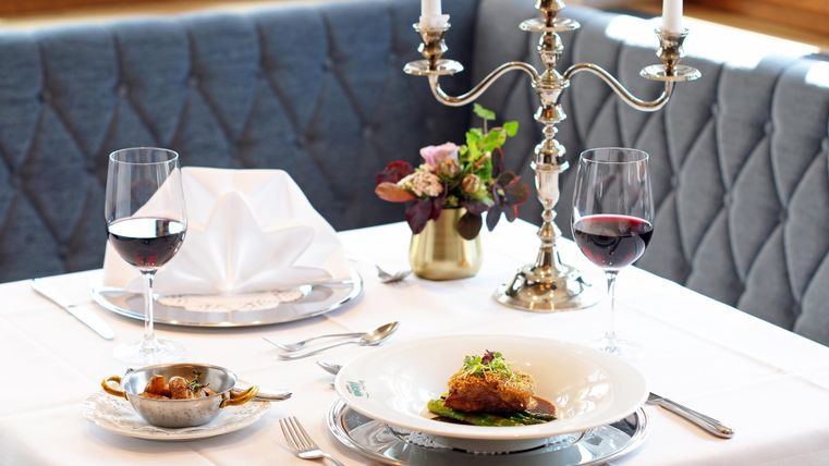 Een elegant gedekte tafel met een mooi gerecht in het midden. Twee wijnglazen en een bloemenarrangement maken het plaatje compleet.