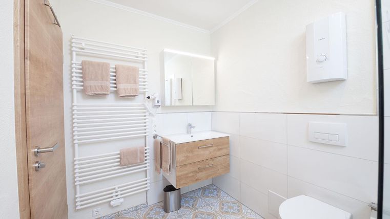 Ein modernes Badezimmer mit einem Holzwaschtisch und einem großen Spiegel. Die Wände sind in neutralen Farben gehalten, und es gibt Heizungsröhren sowie Handtücher in sanften Tönen.