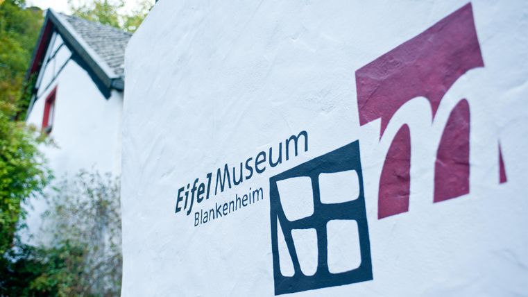 A sign of the Eifel Museum in Blankenheim that adorns the facade of a building. It displays the name of the museum and a modern logo.