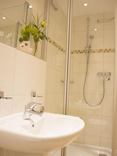 Een moderne badkamer met douche en wastafel. Witte tegels en een plant decoreren de ruimte.