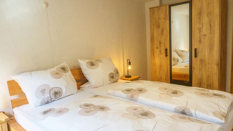 Ein gemütliches Schlafzimmer mit einem Doppelbett und hellen Bettwaren. Einen Holzschrank mit Spiegel und warmem Licht sorgen für eine einladende Atmosphäre.