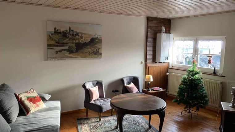 A cozy living room with a nice sofa and two chairs. There is a table in the middle and a small Christmas tree in the corner.