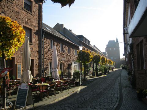 Eine charmante Straße mit historischen Gebäuden und blühenden Pflanzen. Gemütliche Tische laden zum Verweilen ein.