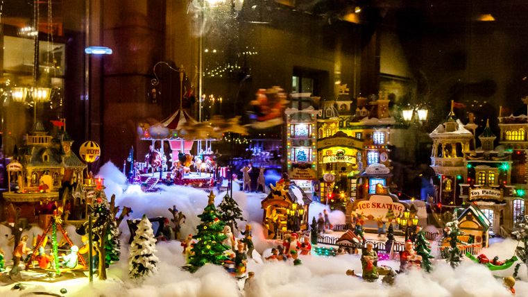 Eine festliche Weihnachtslandschaft mit miniaturem Häusern, Bäumen und Figuren. Die Szene ist von Lichtern beleuchtet und erinnert an eine winterliche Traumwelt.