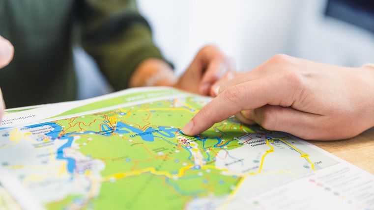 Zwei Personen betrachten eine Landkarte. Eine Hand zeigt auf einen bestimmten Punkt auf der Karte.