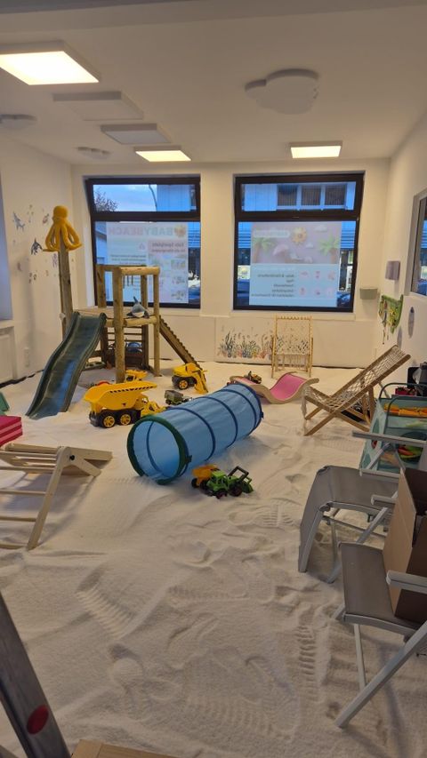 Een speelkamer met een zandvloer en verschillende speeltoestellen. Speelgoed zoals auto's en een tunnel zijn ook aanwezig.