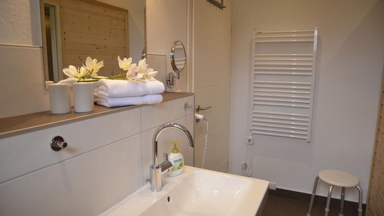 A modern bathroom with a sink and a large mirror. Fresh towels and decorative flowers create an inviting atmosphere.
