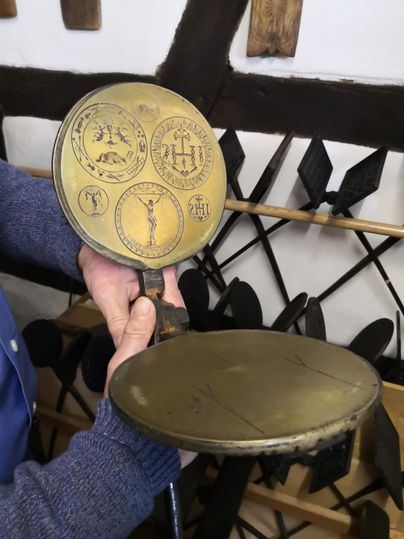 Ein handgefertigter, runder Abdruck aus Metall mit verschiedenen Symbolen. Die Person hält das Stück in der Hand und es gibt eine rustikale Umgebung im Hintergrund.