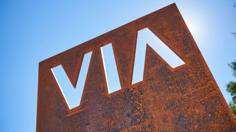 Ein rostiger Schilder mit der Aufschrift "VIA" vor blauem Himmel. Der Schriftzug hebt sich deutlich ab.