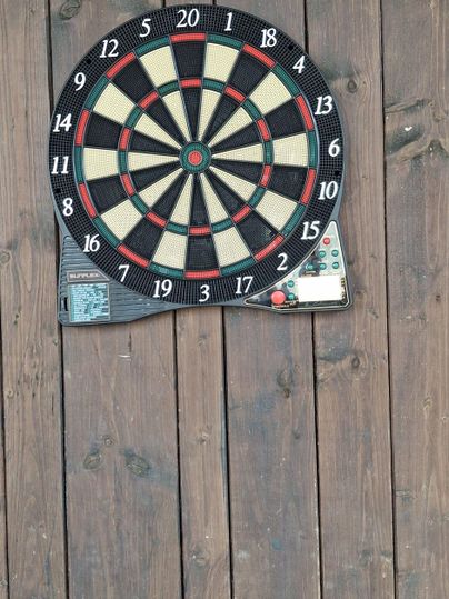 Eine Dartscheibe an einer Holzwand. Die Scheibe hat die typischen Zahlen und Farben.