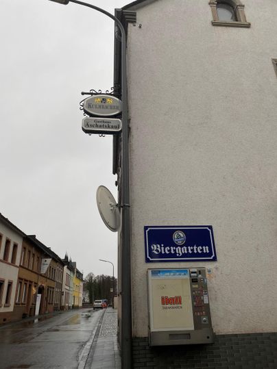 Een straatscène met een biertuinbord en een herberg. De lucht is bewolkt en het regent licht.
