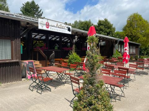 A restaurant with an outdoor area and wooden furniture. Red umbrellas are set up in the square under a clear sky.