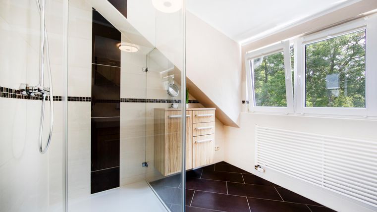 Ein modernes Badezimmer mit einer großzügigen Dusche und Holzschränken. Große Fenster sorgen für viel Tageslicht.