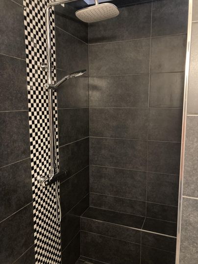 A modern shower with black tiles and a striped black and white pattern. The shower is designed to be simple and stylish.
