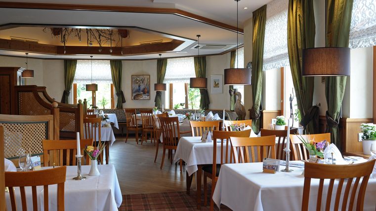 Ein elegantes Restaurant mit weißen Tischdecken und Holzstühlen. Große Fenster lassen viel Licht herein und schaffen eine einladende Atmosphäre.