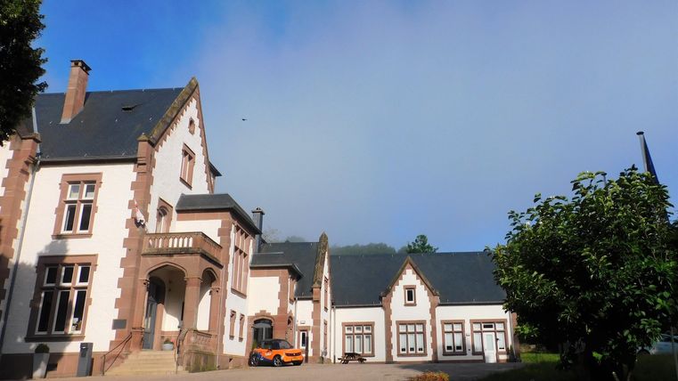 Ein hübsches, historisches Gebäude mit einem modernen Anbau. Der Himmel ist klar und die Umgebung ist grün.