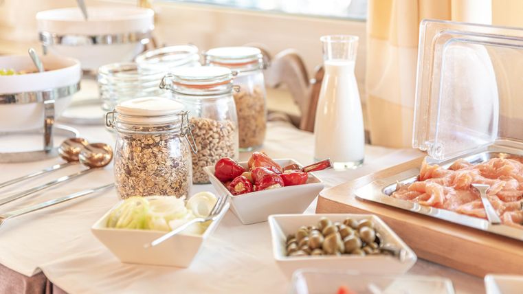 A delicious breakfast table with various food offerings. There is muesli, fresh fruit, and milk in glass carafes.