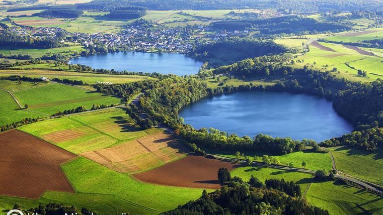 Een luchtfoto van twee meren omringd door groene weiden en velden. Op de achtergrond is een dorp zichtbaar dat omringd is door het mooie landschap.