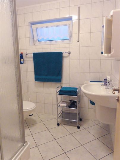 A modern bathroom with bright tiles and a shower. Blue and white towels hang on the towel rack.