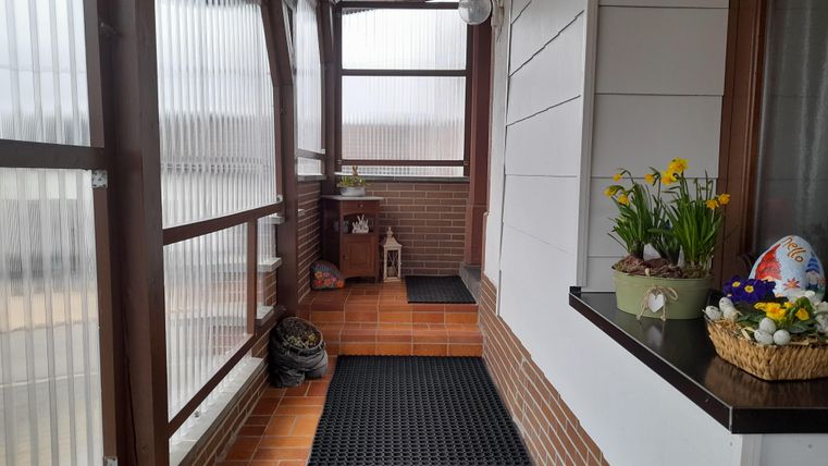 A bright hallway with glass walls and brown tiles. Fresh flowers and an Easter nest are on the windowsill.