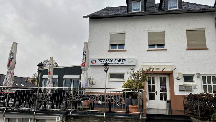 A restaurant named "Pizzeria Party" in a two-story building. The terrace is equipped with sun umbrellas and there are tables outside.