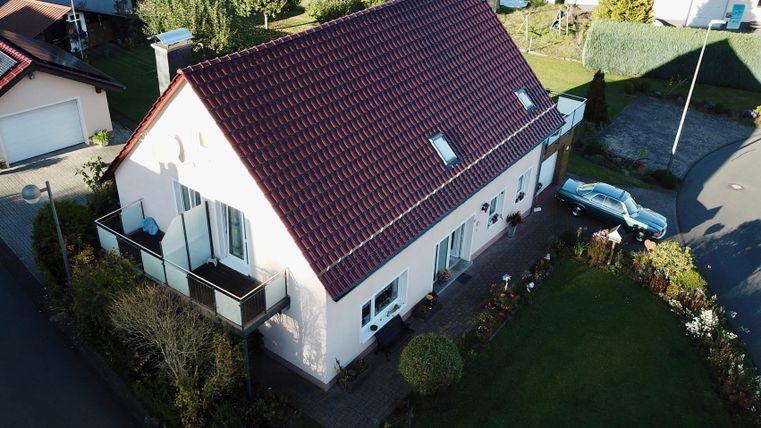 Ein Einfamilienhaus mit rotem Dach und einem gepflegten Garten. Die Umgebung ist ruhig mit weiteren Häusern in der Nähe.
