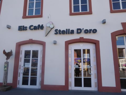 Een café met de naam "Eis Café Stella D'oro". De façade heeft grote ramen en een elegant ontwerp.