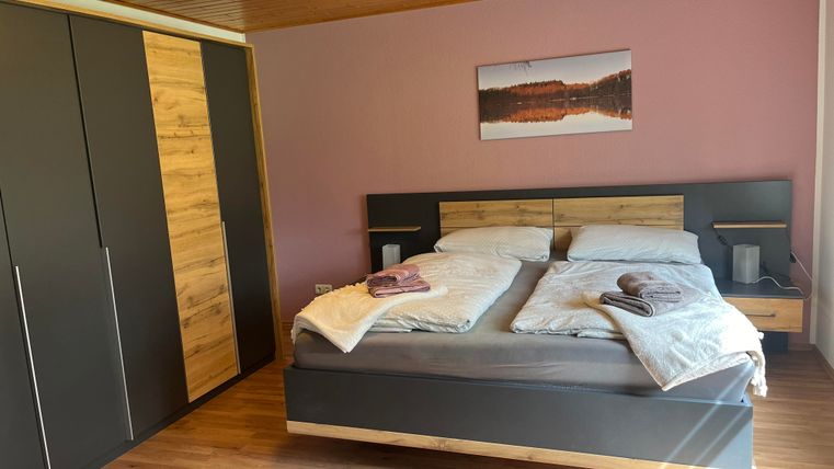 A cozy bedroom with a large double bed and a modern wooden wardrobe. The walls are painted in soft colors, and a picture hangs above the bed.