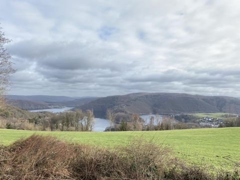 Een schilderachtig landschap met heuvels en een rustige meer. De lucht is bewolkt, maar de groene weide straalt frisheid uit.
