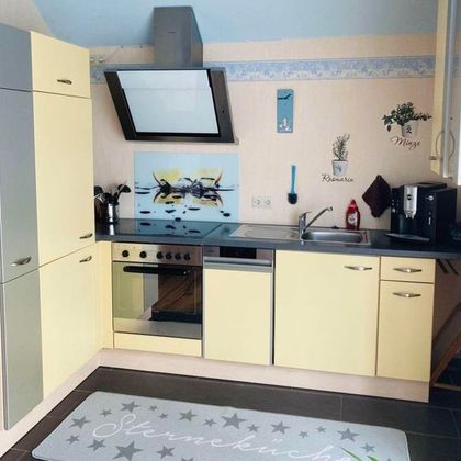 Een moderne keuken met lichtgele kasten en een zwart aanrechtblad. De uitrusting omvat een fornuis, een gootsteen en diverse keukenapparaten.