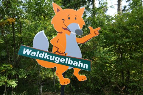 ein lebensgroßer Fuchs mit SSchriftzug Waldkugelbahn zeigt in die Richtung der Waldkugelbahn