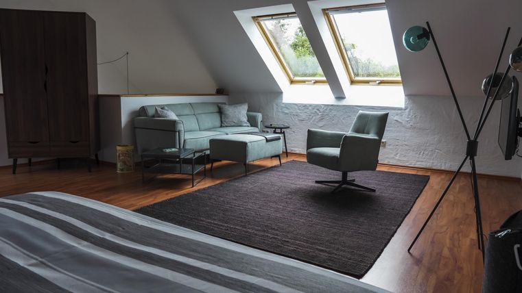 Ein gemütliches Schlafzimmer mit schrägen Fenstern und einem modernen Sessel. Der Raum hat Holzboden und eine ruhige Atmosphäre.